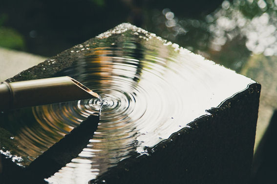 Water gently flowing from a bamboo spout into a reflective stone basin, creating ripples.