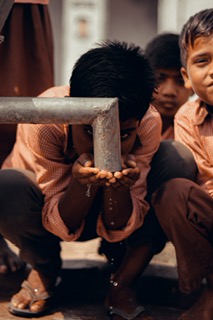 Young boys drinking water from a hand pump