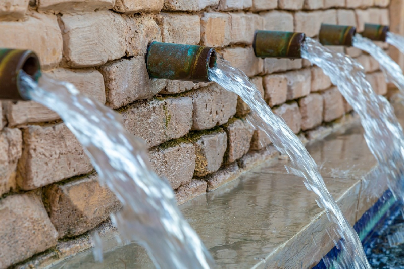 Water flowing from multiple rusty spouts in a stone wall fountain
